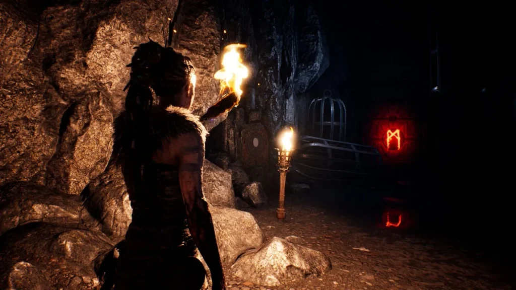Senua holds torch in cave, red rune glows