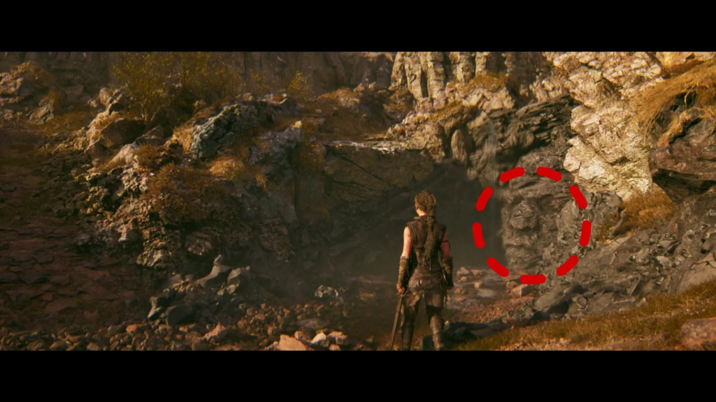 Senua stands near rocky cave entrance in Hellblade