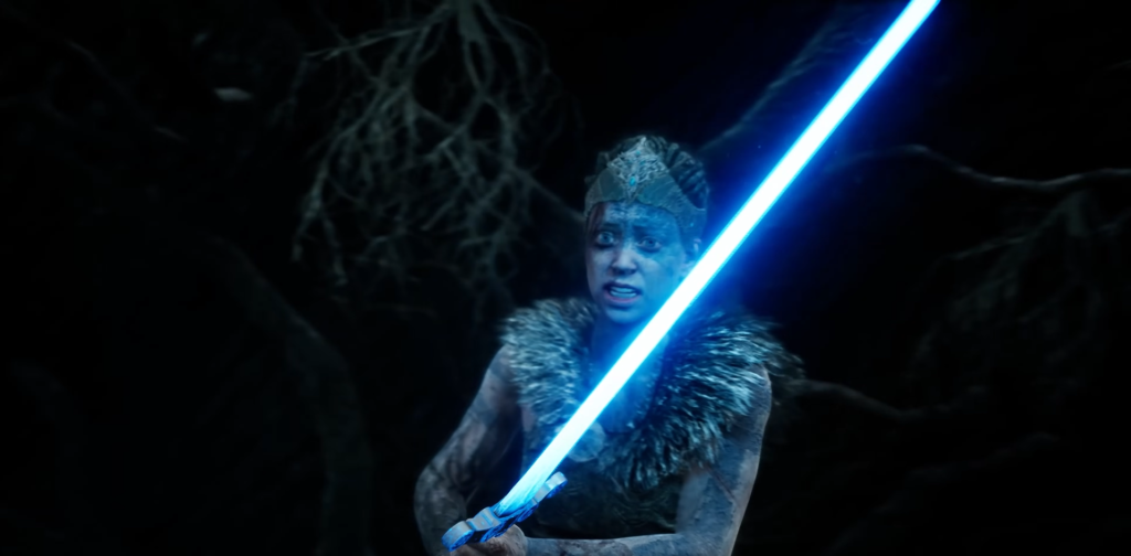 Сенуа из Hellblade держит синий световой меч в пещере