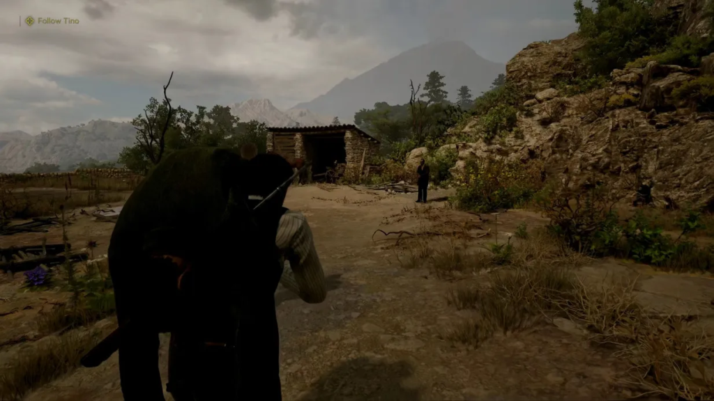Player character carrying body toward shack in mountains
