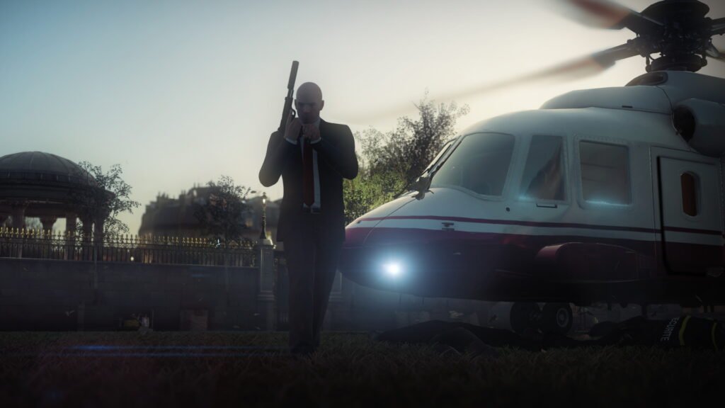 Agent 47 holding rifle beside helicopter on lawn